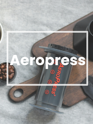 Aeropress coffee maker on a wooden cutting board with coffee beans and a blurred background